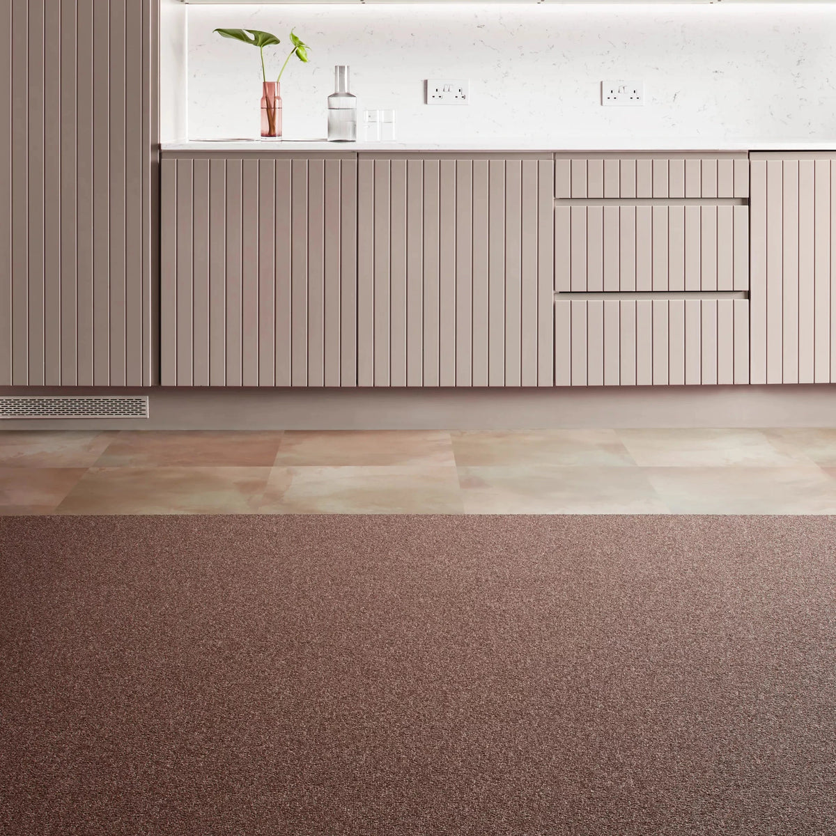 A modern interior scene showing a large textured brown carpet in the foreground, with a contemporary kitchen or storage wall in the background featuring beige ribbed cabinets, a white marble-like counter, and metallic gold panels.